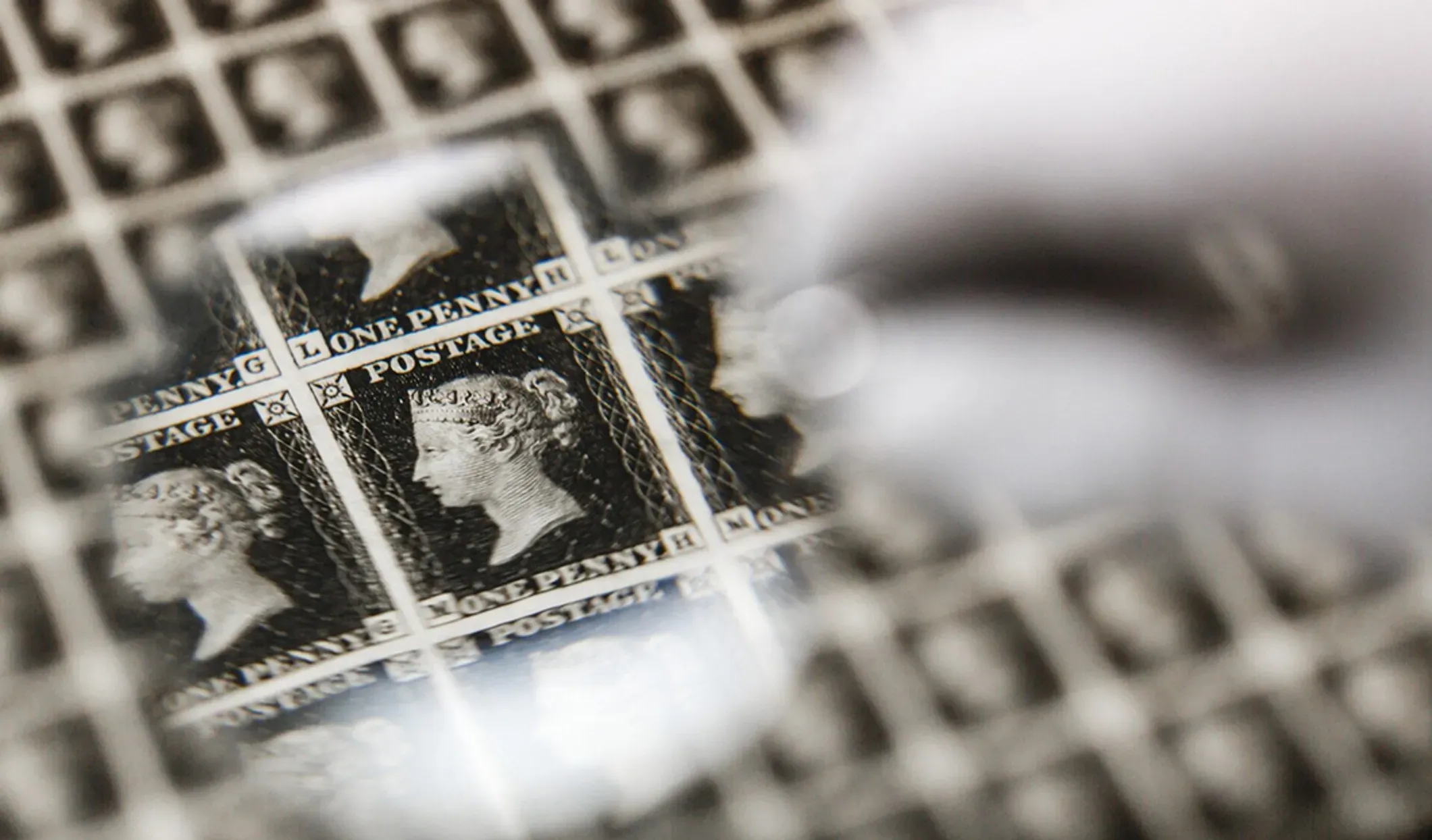 A magnifying glass reveals the engraving and plate details on a sheet of Penny Black stamps.